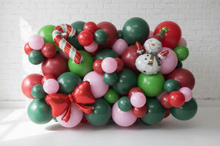 Decorative balloon arch with red, green, and pink balloons, candy cane, and snowman figure on a floor.