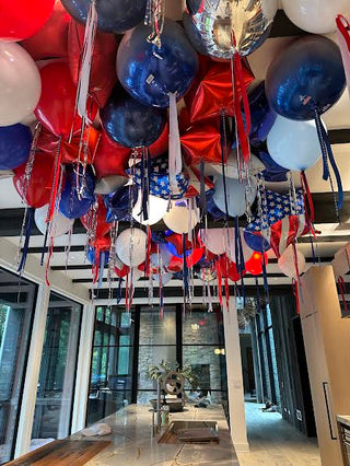 Decorative balloons in red, white, and blue hanging in a room with large windows.