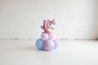 Unicorn balloon surrounded by colorful balloons on a wooden surface with a brick wall background.