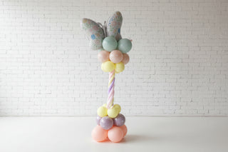 Pastel-colored balloon arrangement with a butterfly decoration against a wooden background