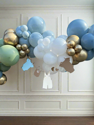 Balloon arch with blue, gold, and white balloons against a paneled wall for baby shower balloon installation