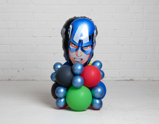 A tabletop centerpiece featuring a superhero character with balloons in red, blue, and green, designed for an action-packed theme party display.