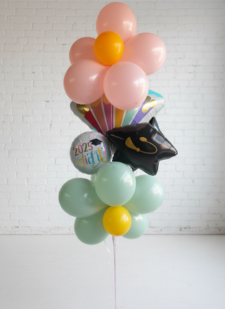A helium balloon bouquet featuring a mix of pastel colors, including pink, yellow, and green, with one balloon having the text 'You did it' printed on it.