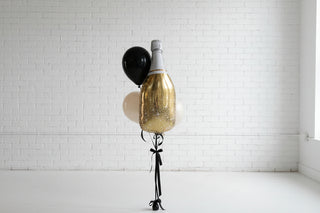 Decorative bottle with gold and black balloons against a white wall for anniversary or engagement party