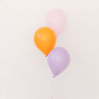 Three balloons in orange, pink, and purple on a light beige background