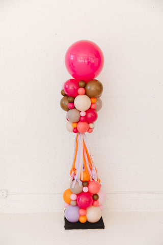 Colorful balloon arrangement with pink, orange, and multicolored balloons on a white background