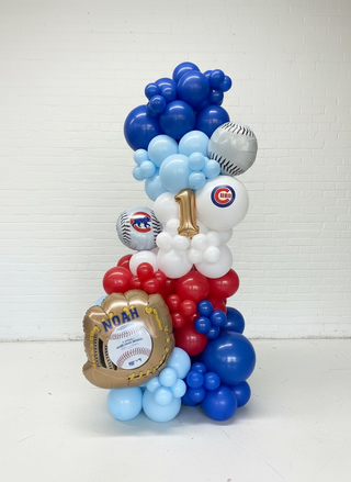 Balloon arrangement shaped like a number '1' with sports-themed decorations in a warehouse setting.
