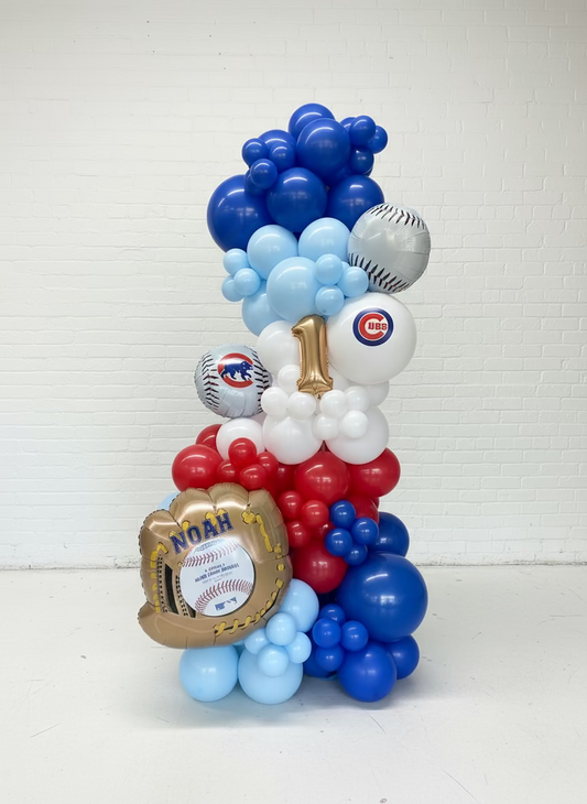 Balloon arrangement shaped like a number '1' with sports-themed decorations in a warehouse setting.