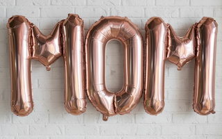 Balloon letters spelling out the word 'MOM' in rose gold color.
