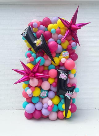 Colorful neon balloon structure with star-shaped balloons and black lightning bolt decorations in front of a house.
