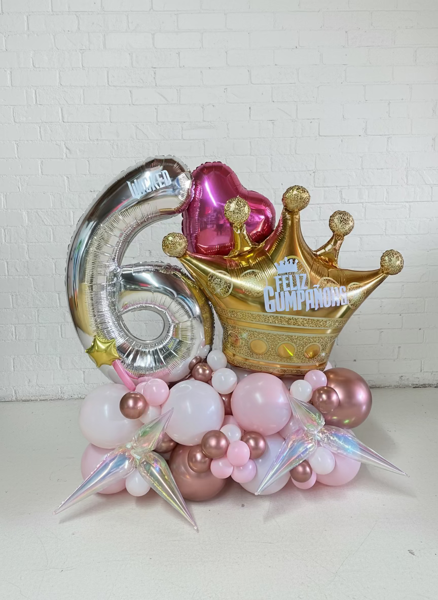 Decorative balloons with numbers, crowns, and hats on a wooden floor against a brick wall.