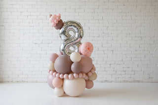 A balloon display featuring a number 2 with surrounding balloons in shades of pink and beige, resembling a dessert platter.