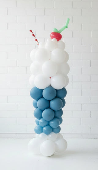 Two balloon displays shaped like milkshakes with candy and cherry toppings, the taller one is 6.5ft and the shorter one is about 3ft.