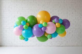 A colorful balloon garland featuring various round balloons in colors green, yellow, pink, blue, and purple, displayed against a light background.