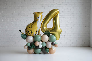 A jungle-themed balloon pedestal featuring a cheetah, with a large gold number 4, surrounded by balloons in shades of green, beige, and gold, and decorative elements like leaves.