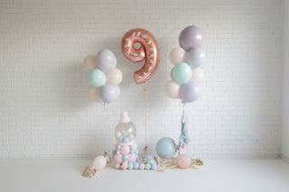 A display featuring a large number 9 balloon, surrounded by smaller round balloons in shades of pink, blue, and beige, along with a gumball machine and various candies.
