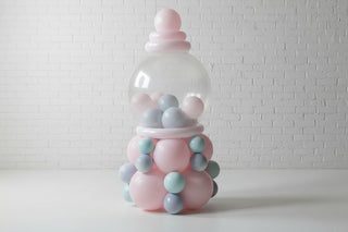 A gumball machine made out of balloons, with a clear dome on top and a base of pink and blue balloons.