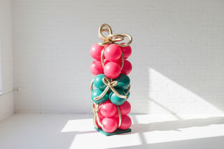 Decorative balloon present stack with pink and green spherical elements on a white surface