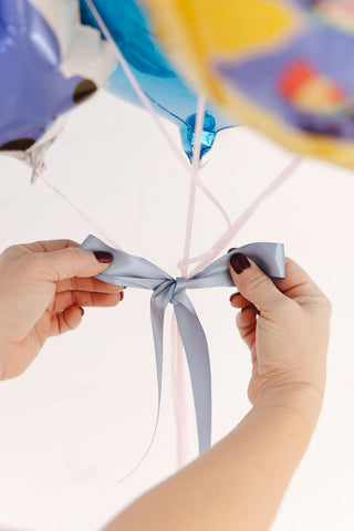 Woman tightening a blue ribbon box on a balloon bouquet showing the attention paid to the finer details of 99 Haus Balloon Decor Services.
