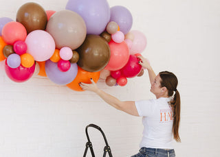 Person arranging colorful balloons against a white wall
