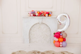 99 Haus Balloons and Decor balloon column with the number 9 balloon on top and a balloon garland on the white fireplace mantle.