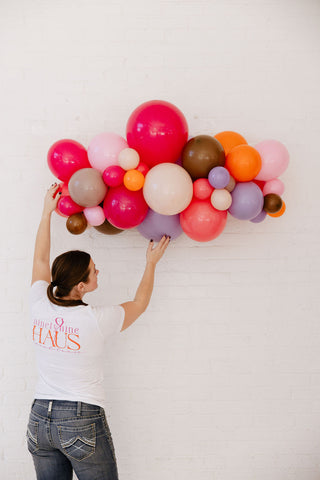 Founder of 99 Haus Balloons and Decor hanging a colorful balloon garland on the wall