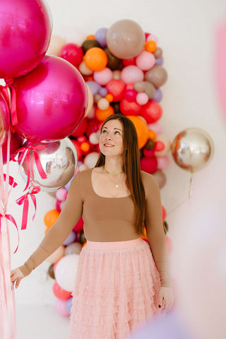 Founder of 99 Haus Balloons and Decor holding pink and silver chrome balloons as she walks in front of a colorful balloon column.