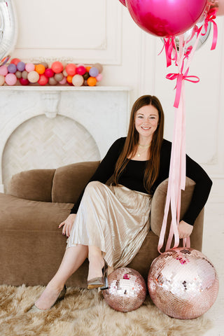 Founder of 99 Haus Balloons and Decor sitting on a beige couch next to two pink disco balls