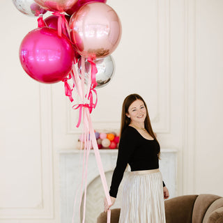 Founder of 99 Haus Balloons and Decor holding helium filled pink chrome balloons and smiliing
