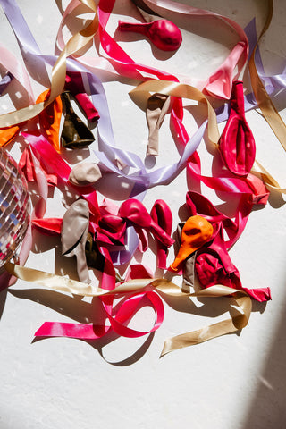 Deflated balloons and ribbons in bright pink and beige tones next to a disco ball