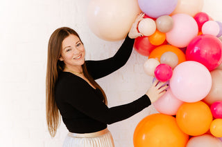 Founder of 99 Haus Balloons and Decor constructing a balloon arch made of bright pink and orange balloons