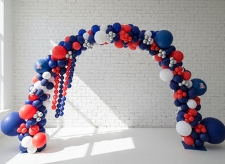 A decorative balloon arch featuring a mix of red, blue, white, and silver balloons with a few foil accents, set up indoors.