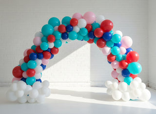A balloon arch featuring a collection of latex and foil balloons, arranged organically in an indoor setting. 