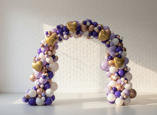 A balloon arch featuring a collection of latex and foil balloons, arranged organically in an indoor setting. 