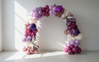 A balloon arch featuring a collection of latex and foil balloons, arranged organically in an indoor setting. 