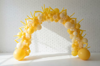 A balloon arch featuring a collection of latex and foil balloons, arranged organically in an indoor setting. 