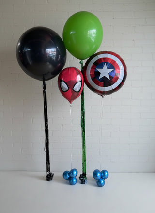 A set of balloons with superhero designs including Captain America, Spider-Man, and others from the Marvel universe. The balloons are on sticks and attached to weights.