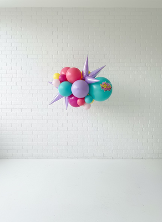 Colorful balloon arrangement with a 'Woah' balloon under a black and white striped canopy.