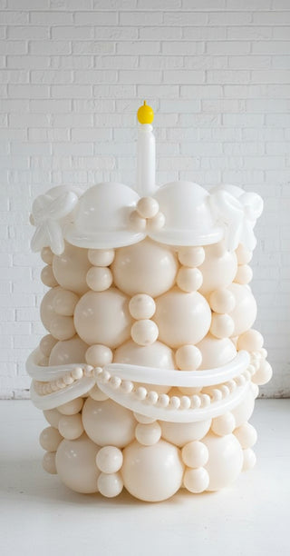A balloon cake designed to look like a tiered birthday cake with white balloons and decorations, with a single candle on top.