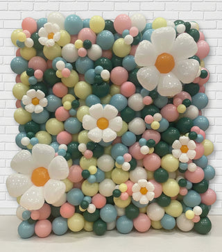 Colorful balloon arrangement with flower shapes against a white brick wall.