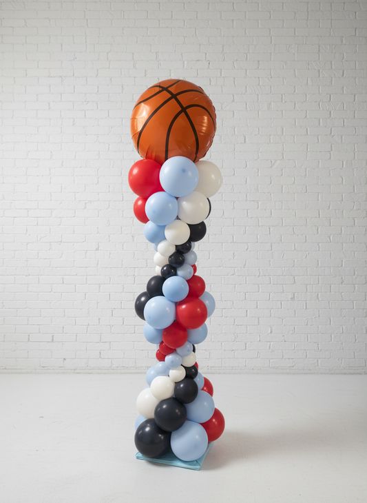 A balloon bubble column with a basketball at the top, featuring a spiral pattern of multicolored balloons in red, white, and blue shades.