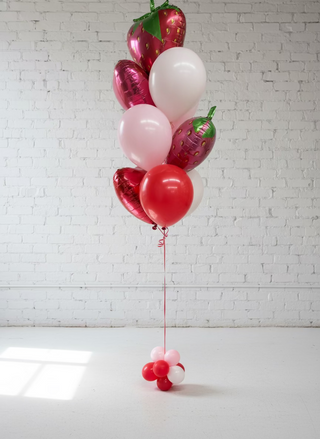 A helium balloon bouquet arranged in the shape of a fruit, predominantly red and white in color, with a decorative ribbon at the bottom.