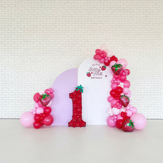 A berry-themed party backdrop with red and pink balloons