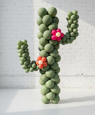 A life-sized balloon cactus decoration with green bodies and two artificial flowers in pink and orange colors.