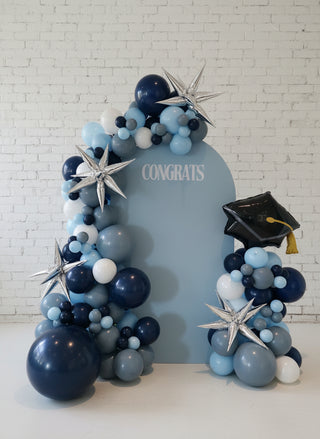 A custom-designed event backdrop featuring an arch of balloons in various shades of blue and silver, with decorative elements and the word 'CONGRATS' displayed.