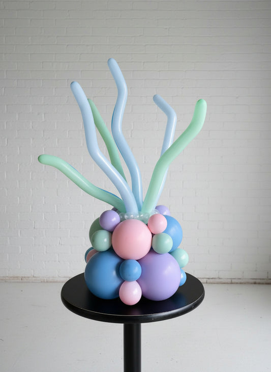 A centerpiece featuring blue, pink, and green balloon coral structures with a brick wall in the background.