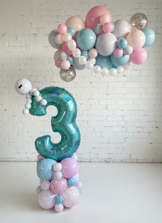 A decorative balloon display featuring a large number 3 with a deep sea theme, including blue, pink, and white balloons, and an underwater creature figurine.