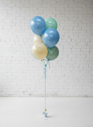 A bouquet of balloons with a mix of blue, gold, and green colors, tied together with string against a wall with paneling.