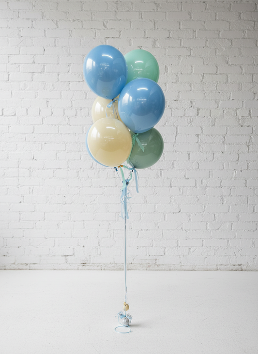 A bouquet of balloons with a mix of blue, gold, and green colors, tied together with string against a wall with paneling.