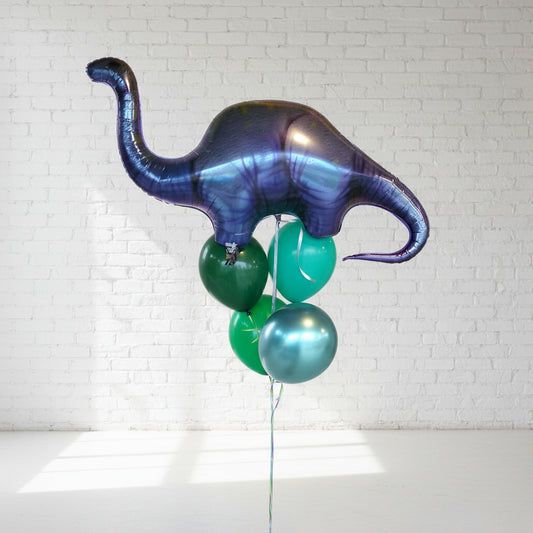 A helium balloon bouquet featuring a large dinosaur shape with smaller round balloons in shades of green and blue, positioned against a light background.